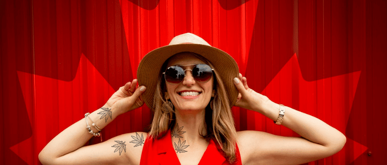 workplace law for Cannabis Users | Woman with cannabis leaf tattoos smiling in front of a curtain with the Canadian Maple Leaf